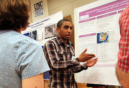 Ronald Lipscomb tells two people about his research as he stands in front of his research poster. 