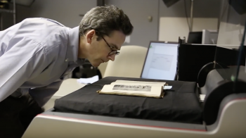 Person looks over a historic book as it is laying on a document scanner.