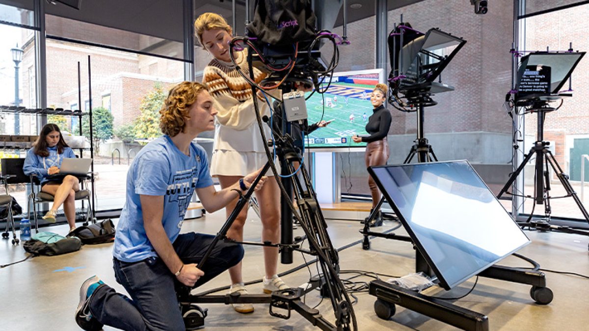 Two students working together by a video camera inside of a TV studio.