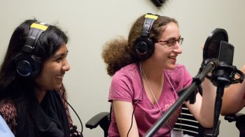Two young women in the Girls talk Math program wear headphones and talk into a microphone.