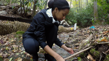A student stands in a creek while conduct research.