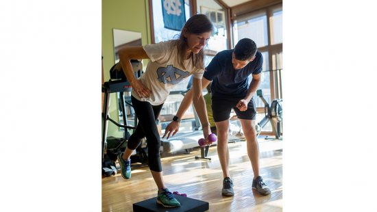 Woman in Carolina t-shirt balances with weights while trainer directs her