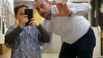 A child holds a cell phone while a man points.