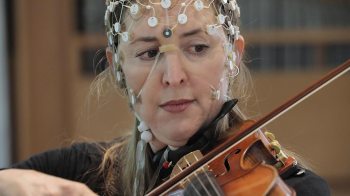 A woman plays the violin with sensors on her head.