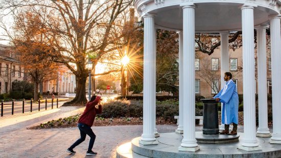 A student poses for a photo by the Old Well.