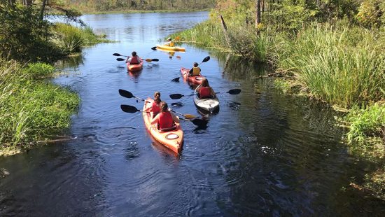 Student paddle kayaks down a river.