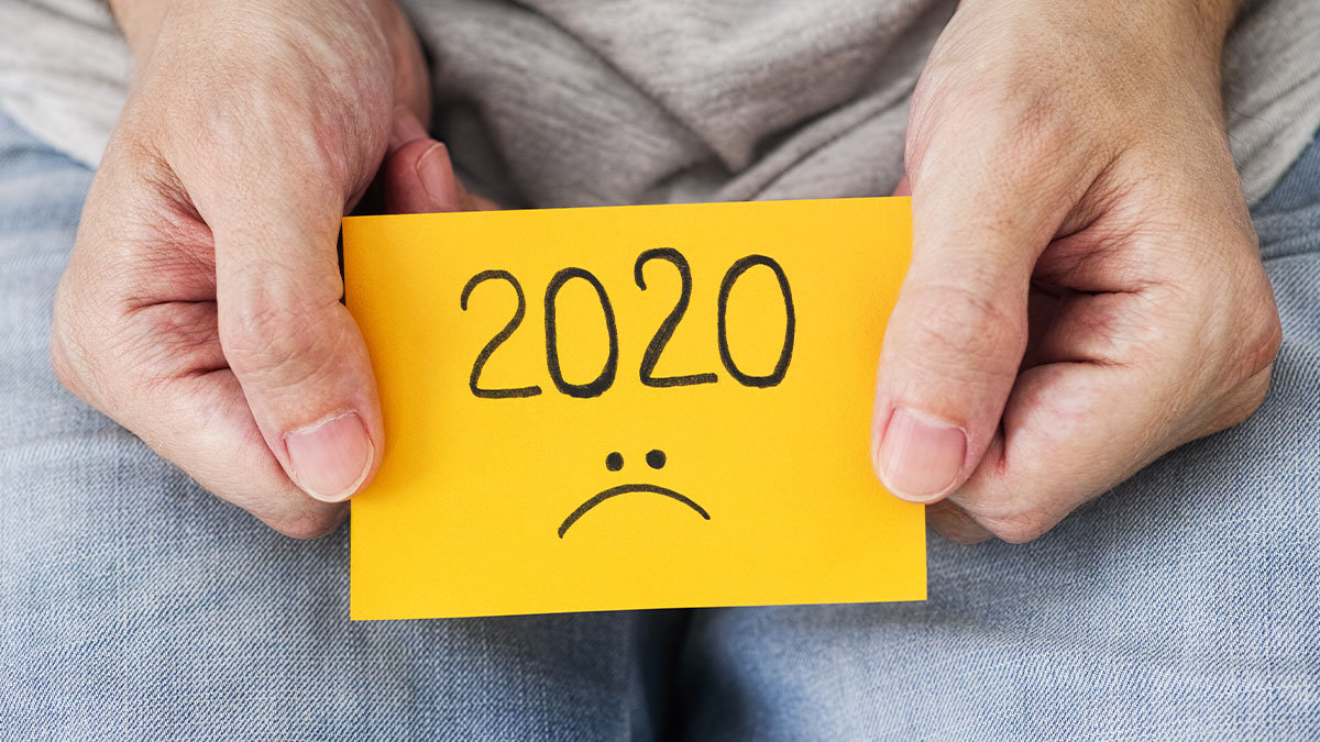 A person holds a post-it note with 2020 and a sad face drawn on it.