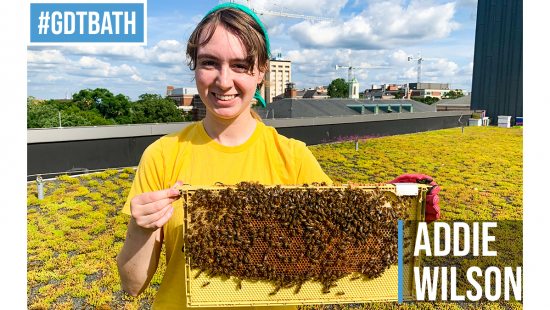 Photo of Addie Wilson on the roof of the Fedex Center holding a hive of bees.