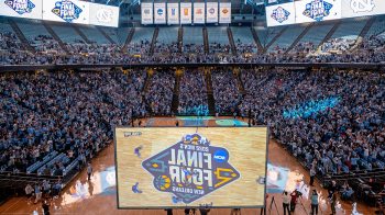 A large screen playing the NCAA tournament in front of thousands of people sitting in the stands of the Dean Smith Center.