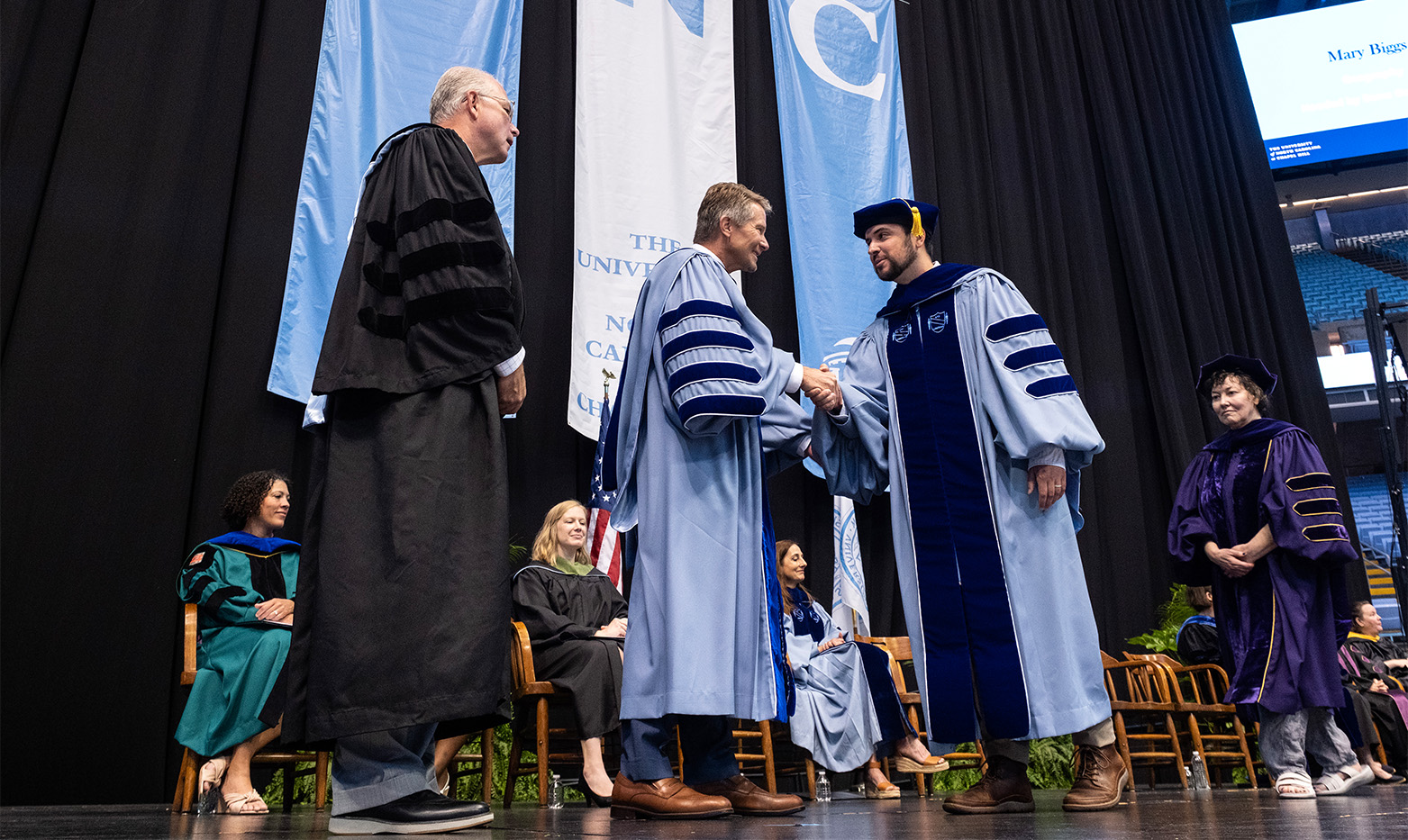 A doctoral graduate shakes hands with the chancellor on stage.
