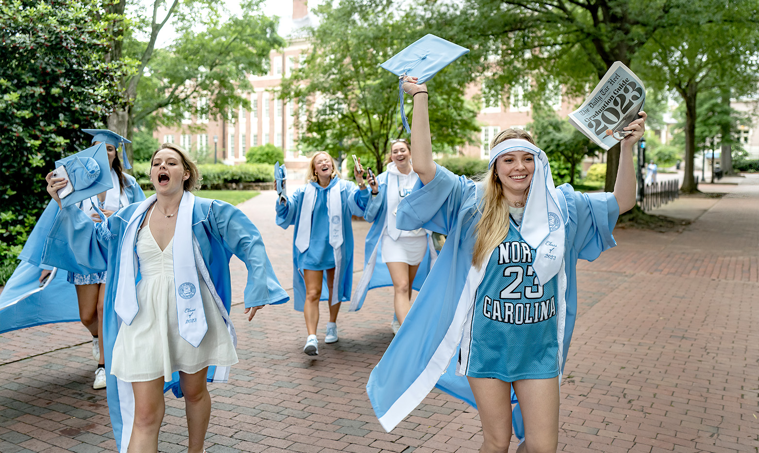 Students running toward Kenan Stadium in cap and gowns.