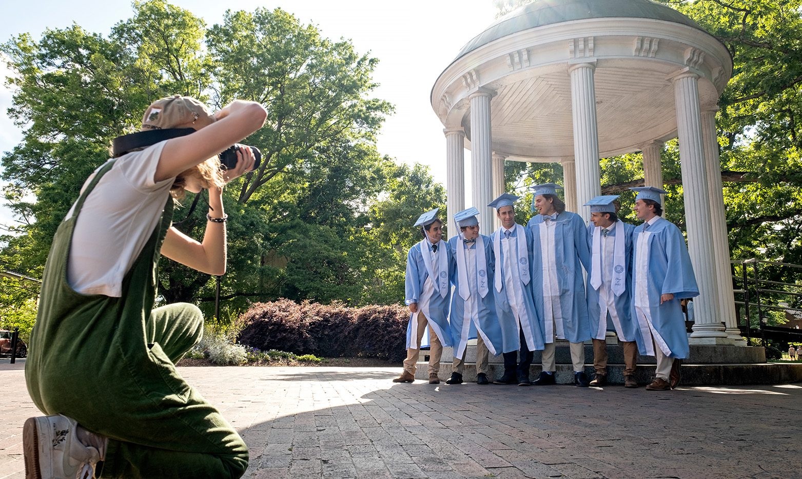UNC students in graduation regalia pose together by the Old Well.