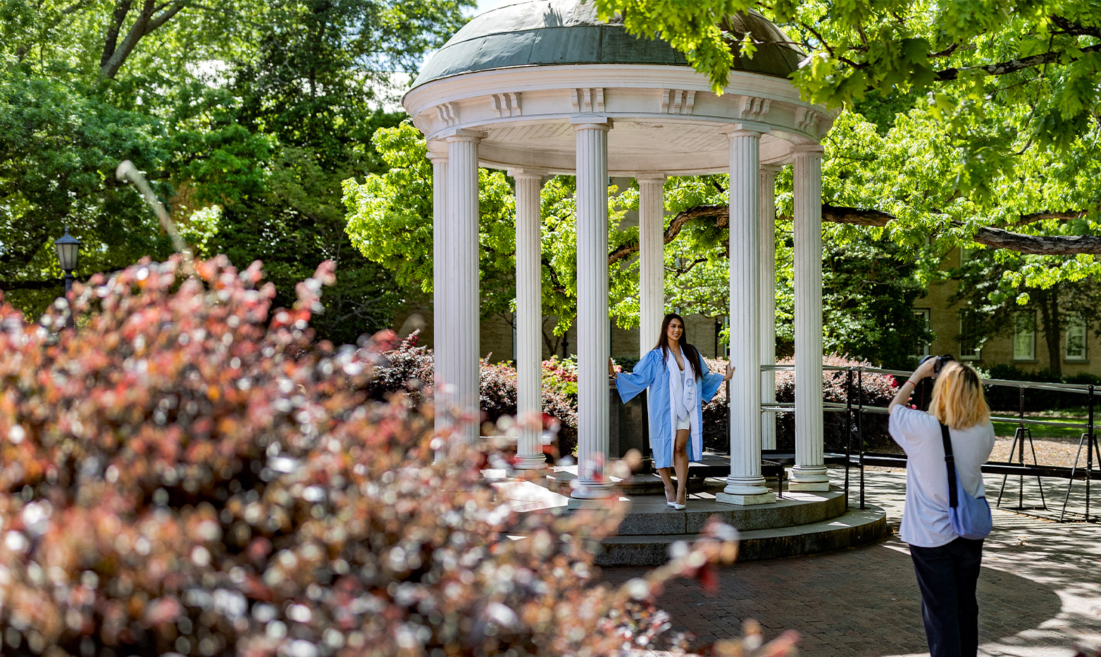 A UNC student poses by the old well in graduation regalia.
