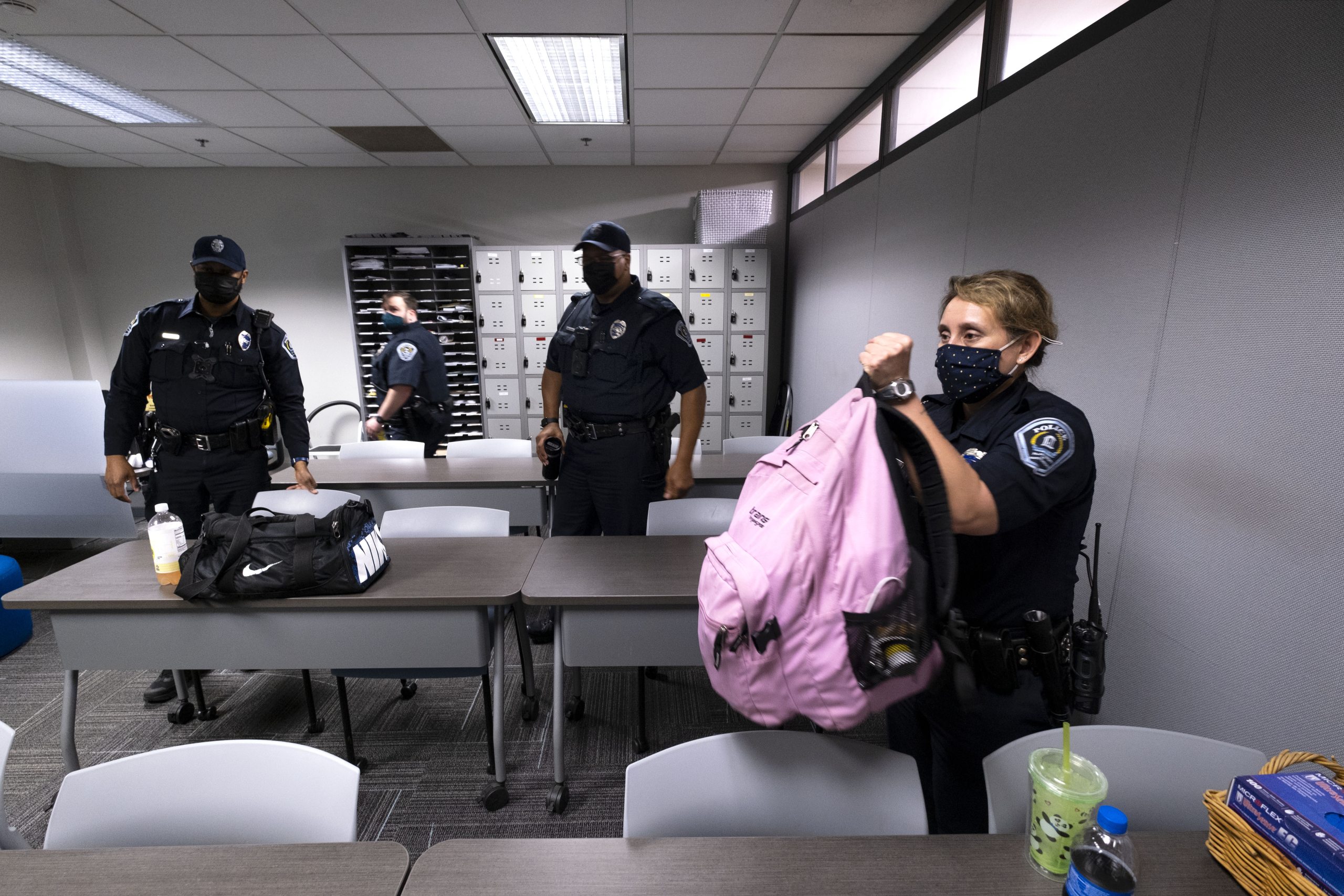 Female police officer lifting large pink book bag, with three male officers in background. All wear Covid masks.