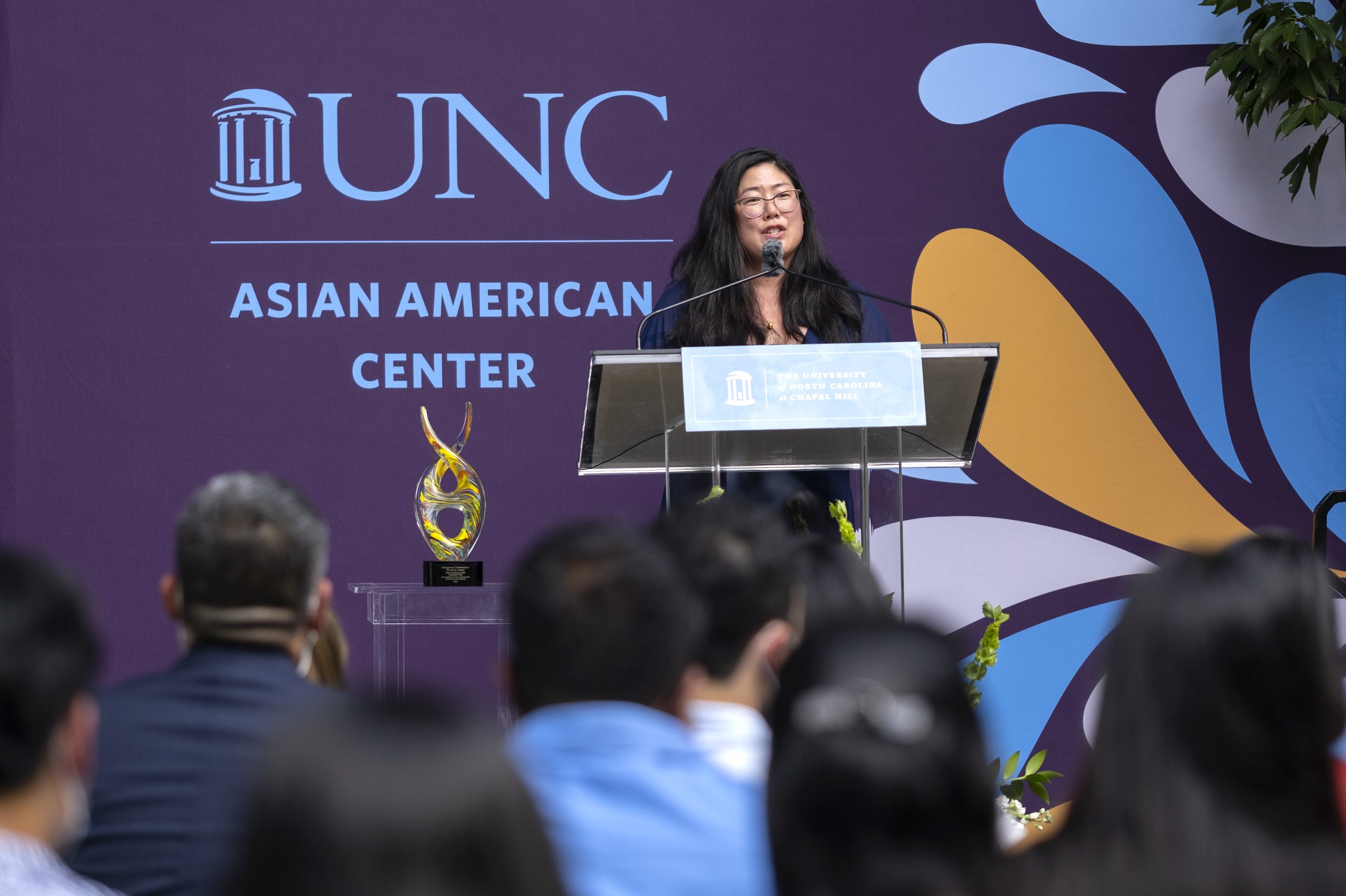 Asian American woman standing at a lecturn outside and addresses a crowd.