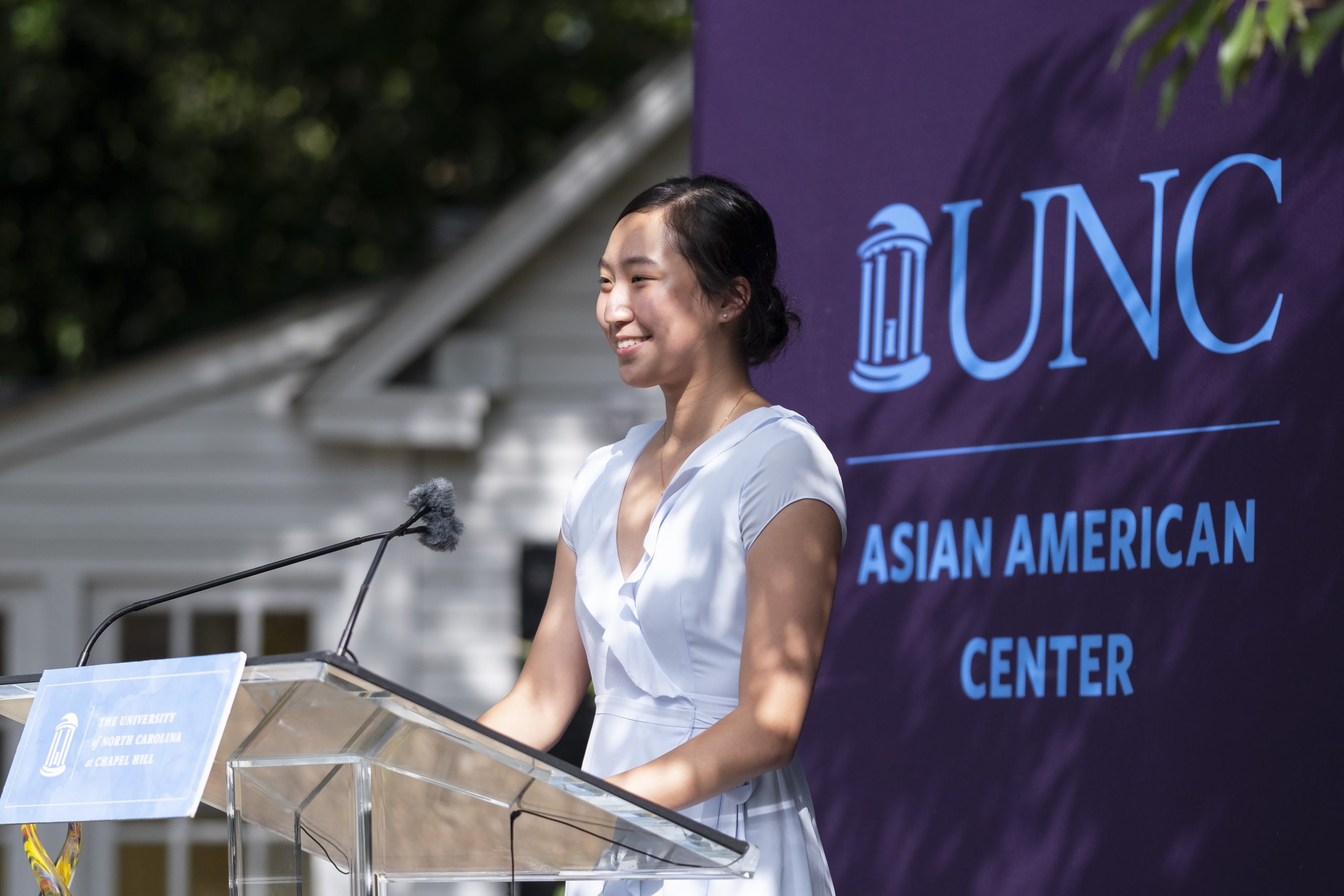 Asian American woman in white dress smiling standing at a lecturn.
