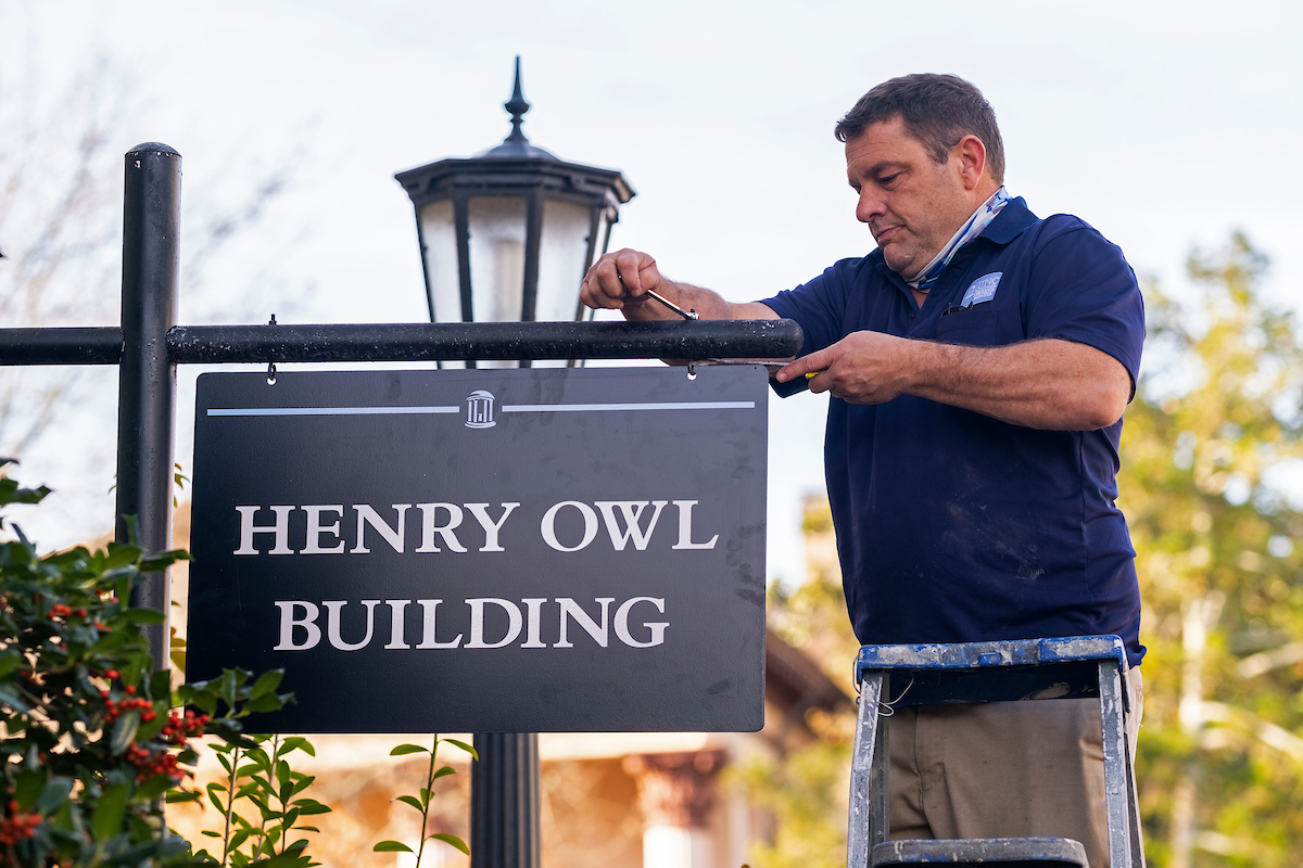 On Dec. 3, Josh Clark, with UNC Facilities, installs the new pedestrian sign for the Henry Owl Building, seen here, and for McClinton Residence Hall.