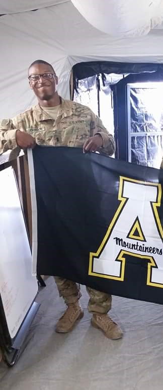 Daniel Johnson in Army uniform holding Appalachian State University flag.