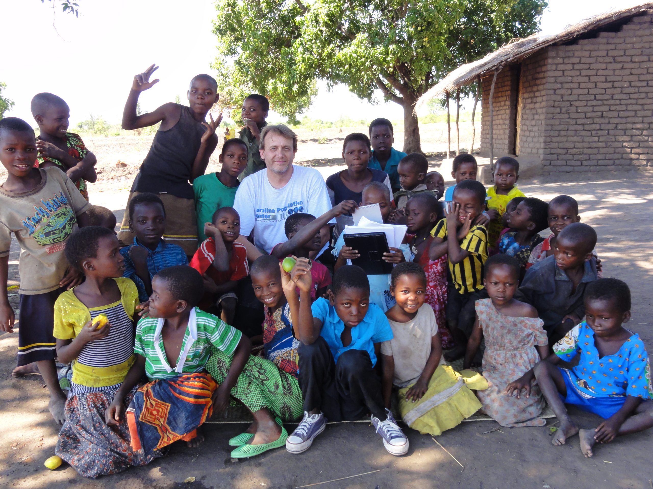 White man posing with two dozen Black children in Malawi.
