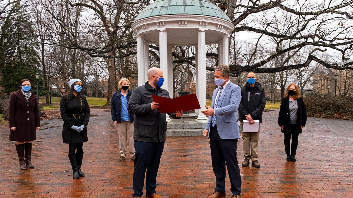 Chancellor Guskiewicz and employees are presented a certificate in front of the Old Well