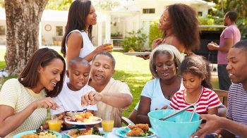 A multigenerational Black family gathers around a table of summertime food.