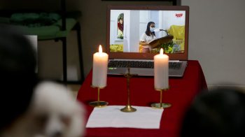 Two candles lit in front of a laptop displaying a viewing of a religious service.