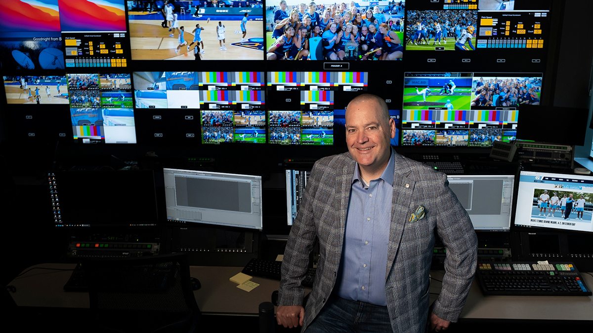 Ken Cleary in control room with a dozen monitors behind him showing UNC sports teams in action.