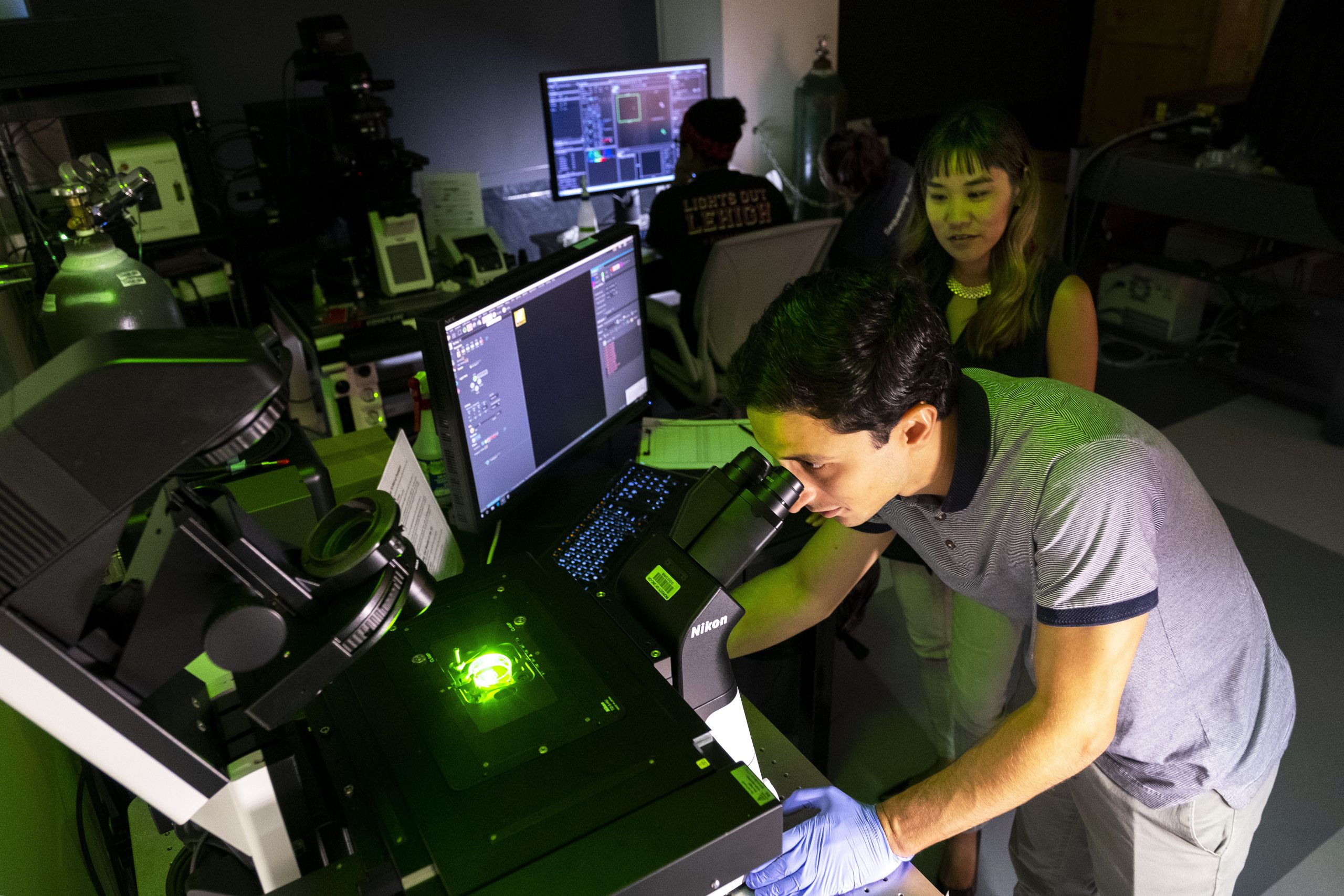 Michelle Itano, Director of the UNC NeuroscienceMicroscopy Core Facility, watches Hernán Méndez, a UNC graduate research assistant., work on a microscope