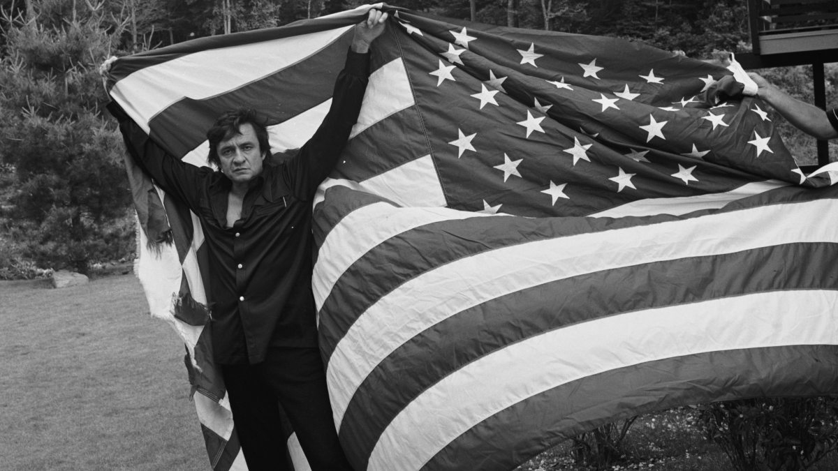 black and white photo of Johnny Cash holding an American flag over his head