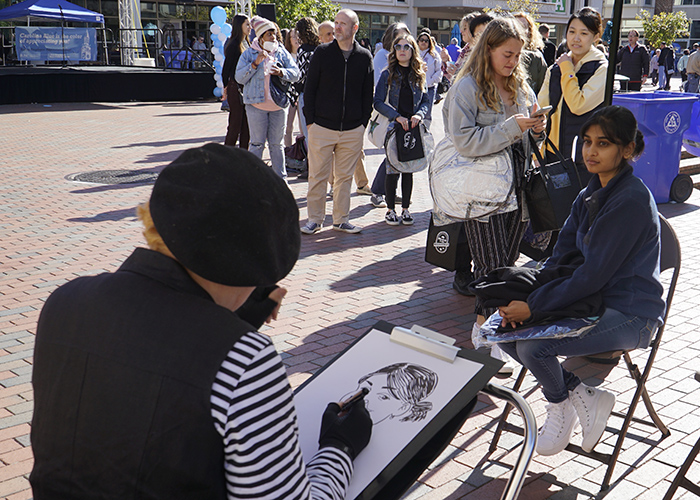 A caricaturist draws a picture of a Carolina employee with a long line of people waiting behind her.