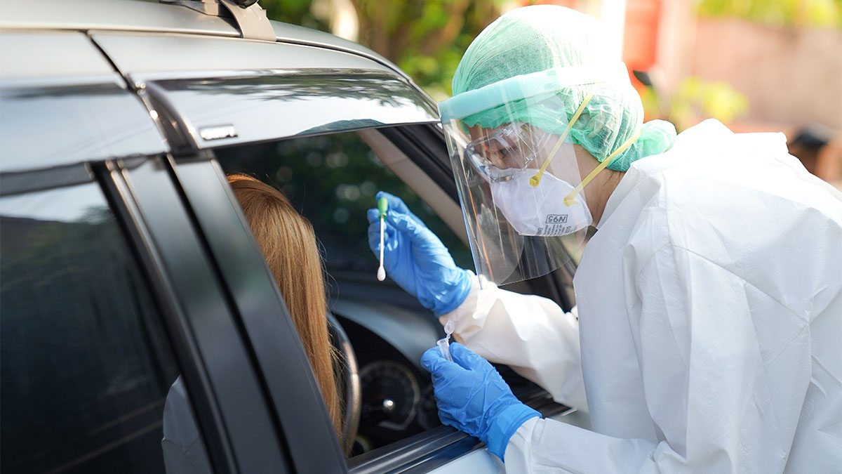 A person in a mask and plastic face shield offering COVID swab test to passenger in car.|No-Cost COVID-19 Testing poster