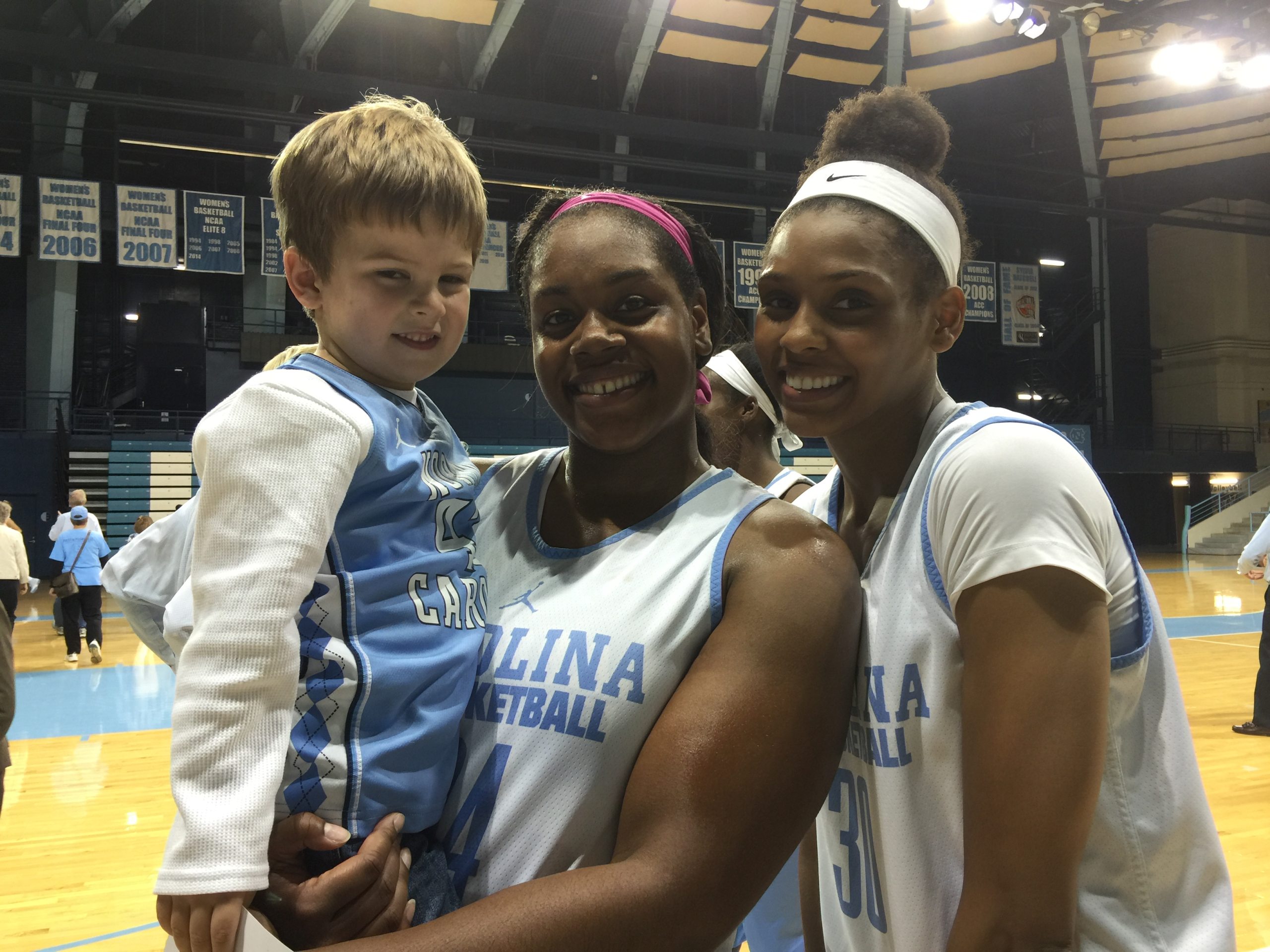 Logan Anderson held by two Carolina women's basketball players after a game.