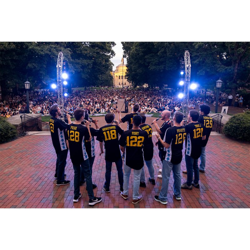 An a cappella group performing in front of South Building facing an audience on Polk Place.