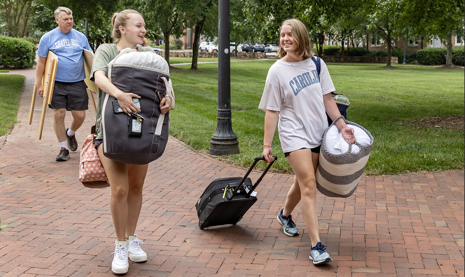 Two women students talking to one another while carrying move-in goods.