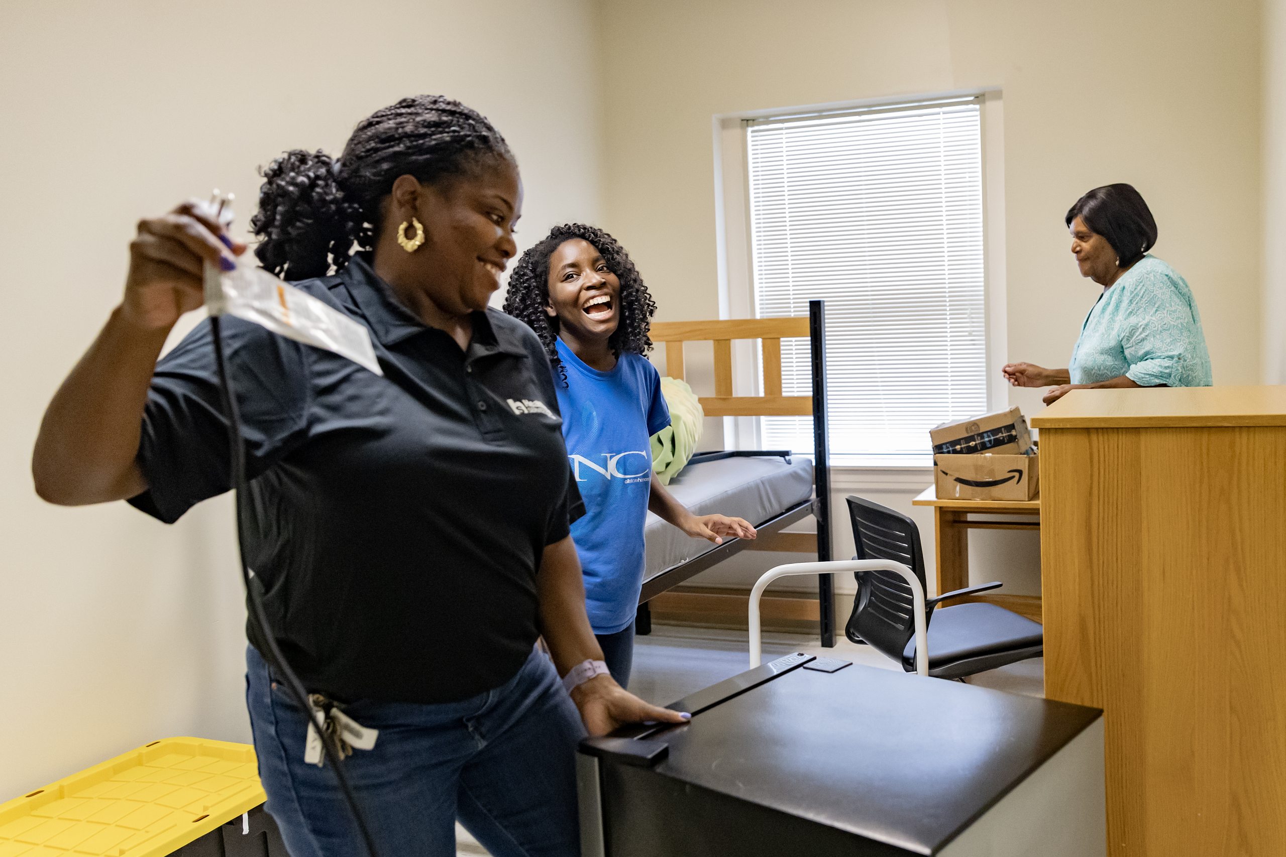 A student, her mother and grandmother smiling and laughing as they set up a dorm room.