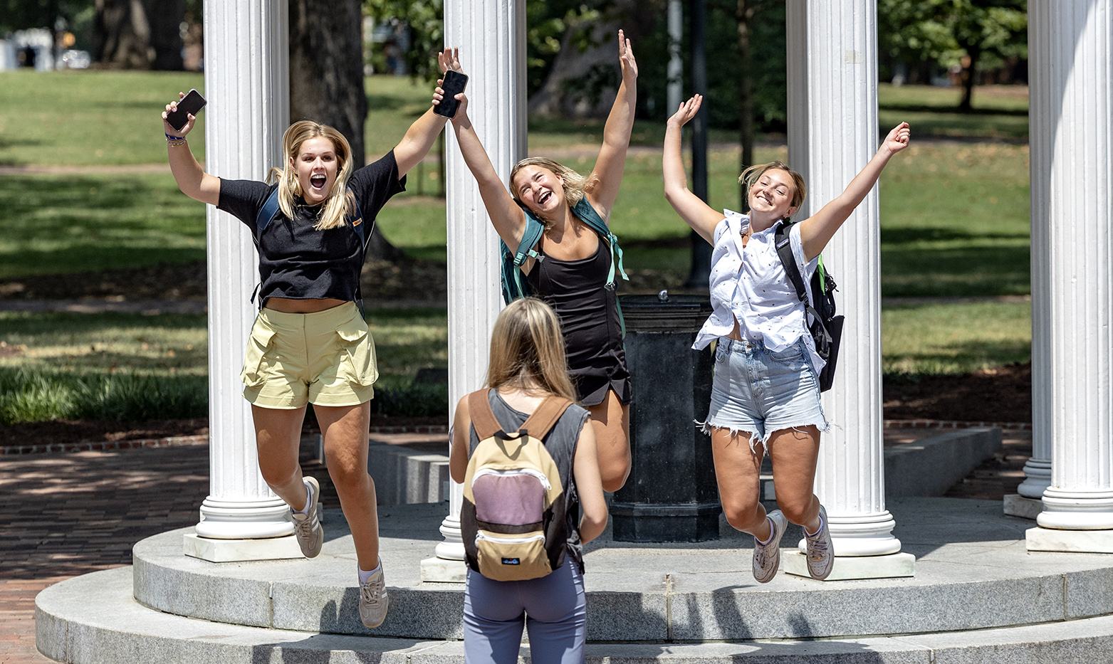 Three students jumping simultaneously while getting their picture taken in front of the Old Well on the campus of UNC-Chapel Hill.