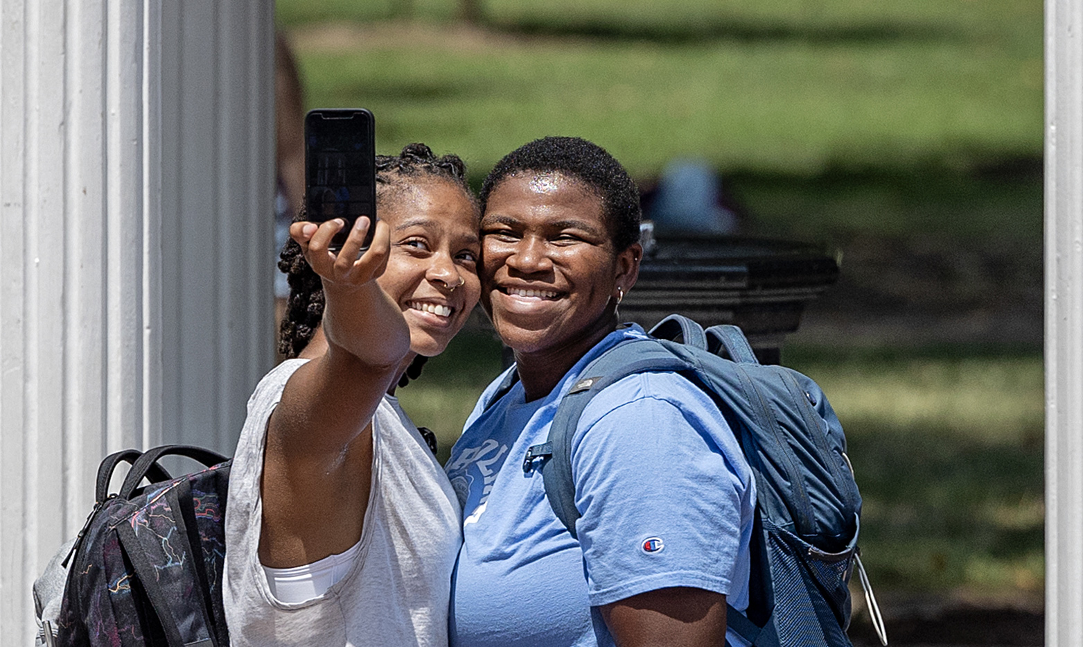 Two students smiling while taking a selife in front of the Old Well.