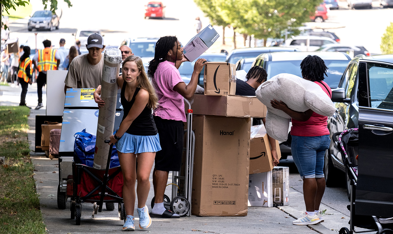 Students collecting items from cars and transporting move-in materials on a sidewalk.