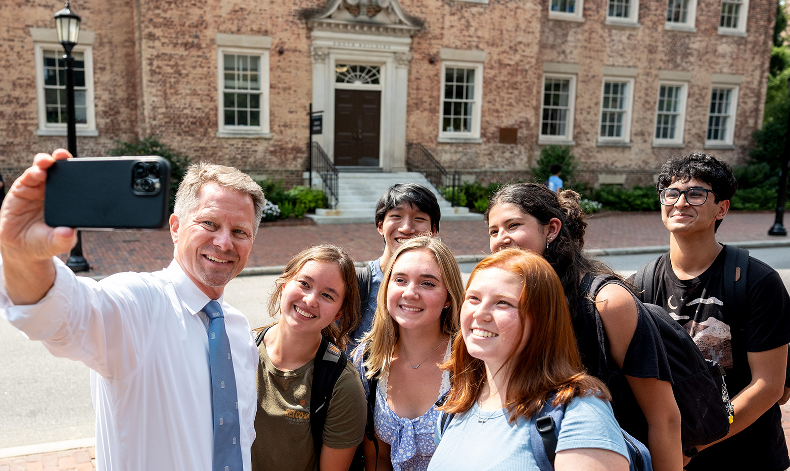 A man, UNC-Chapel Hill Chancellor Kevin M. Guskiewicz, taking a selfie with five students.
