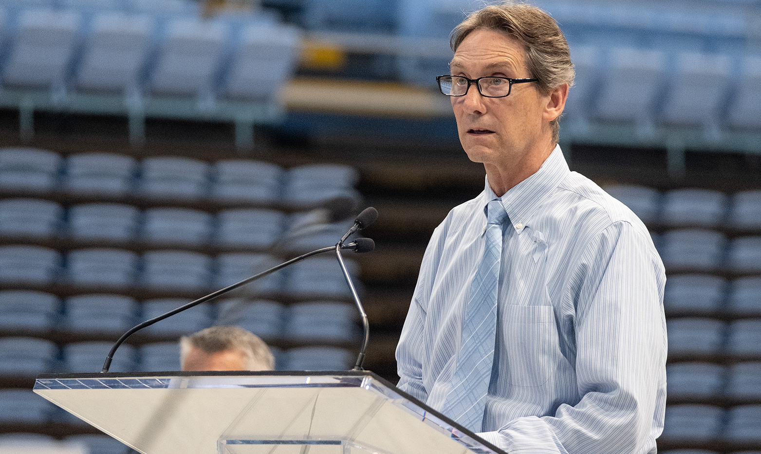 A man, Jim White, speaking at a podium in an arena at a vigil.