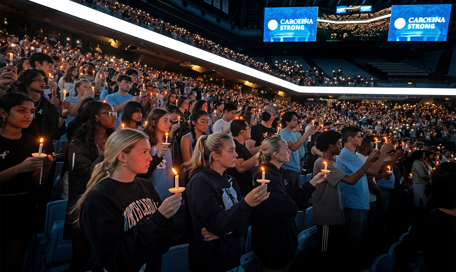 A crowd of people holding candles in an arena at a vigil.