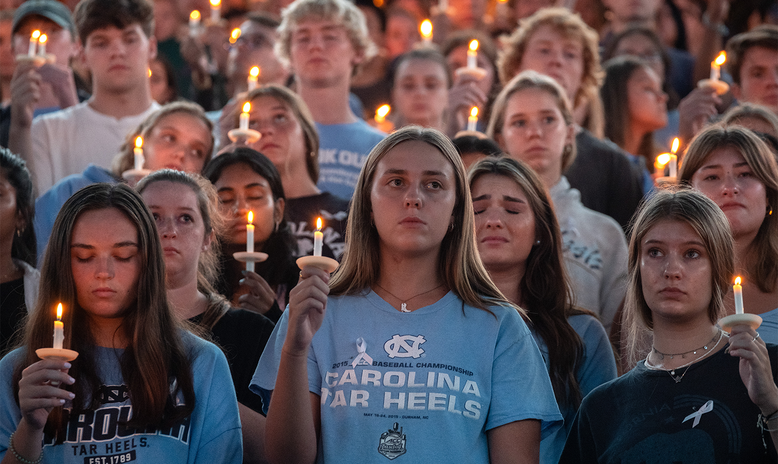 A crowd of people holding candles in an arena at a vigil.
