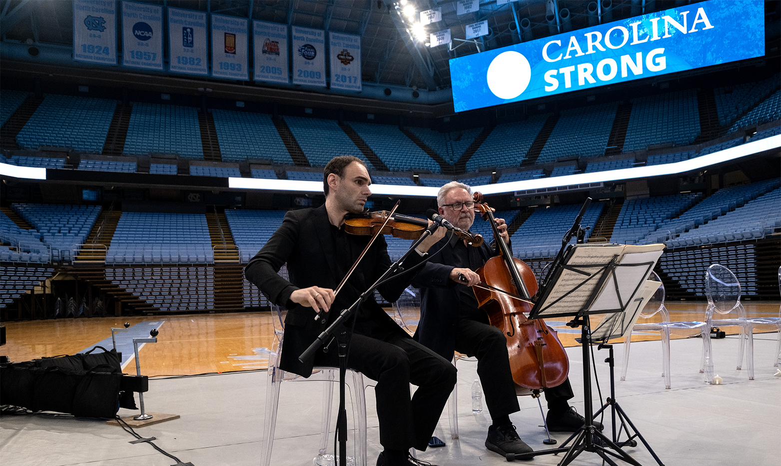 Two men playing the cello and violin in a large arena at a vigil.