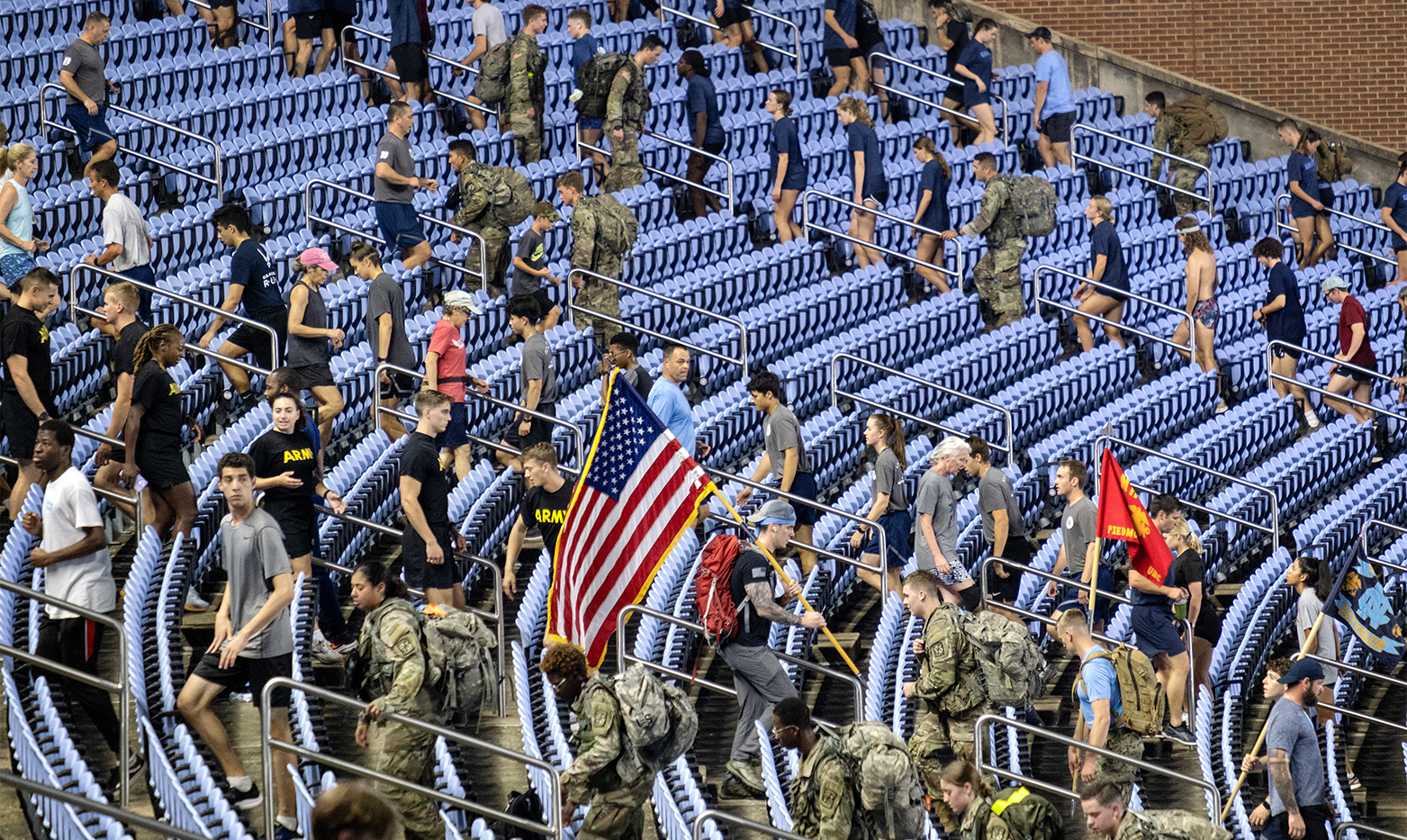 A large group of people, some dressed in military fatigues and some holding flags, running and walking up and down stadium stairs.