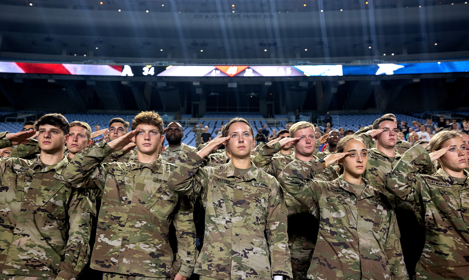 A group of military members in stadium seats saluting.