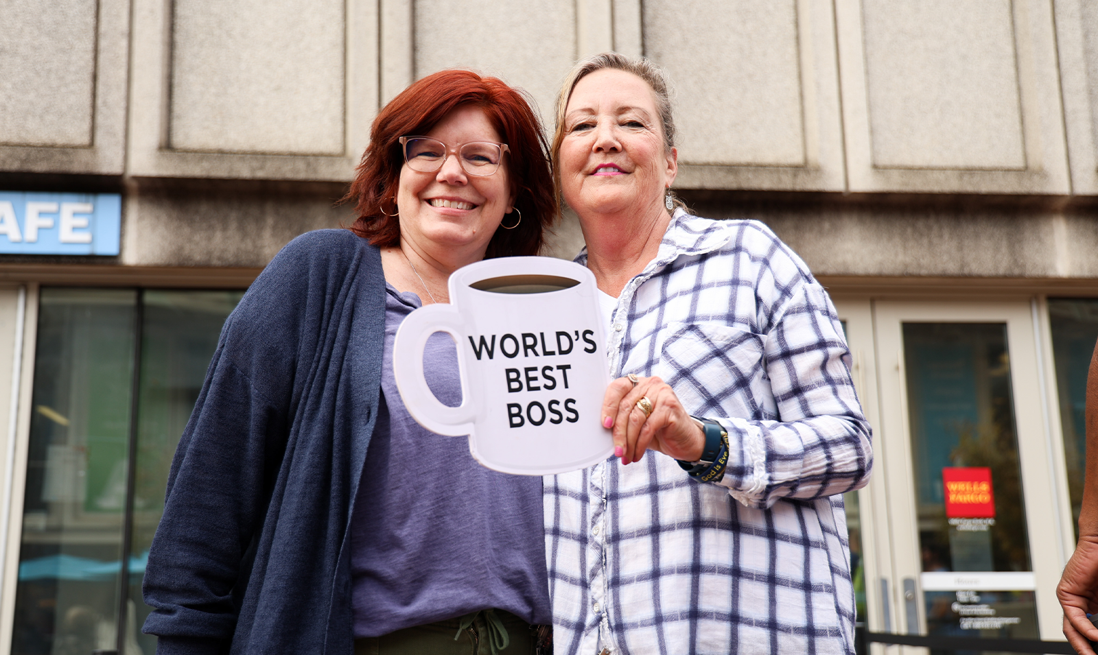 Two women posing for a photo. One is holding a large cutout of a coffee cup with text reading 