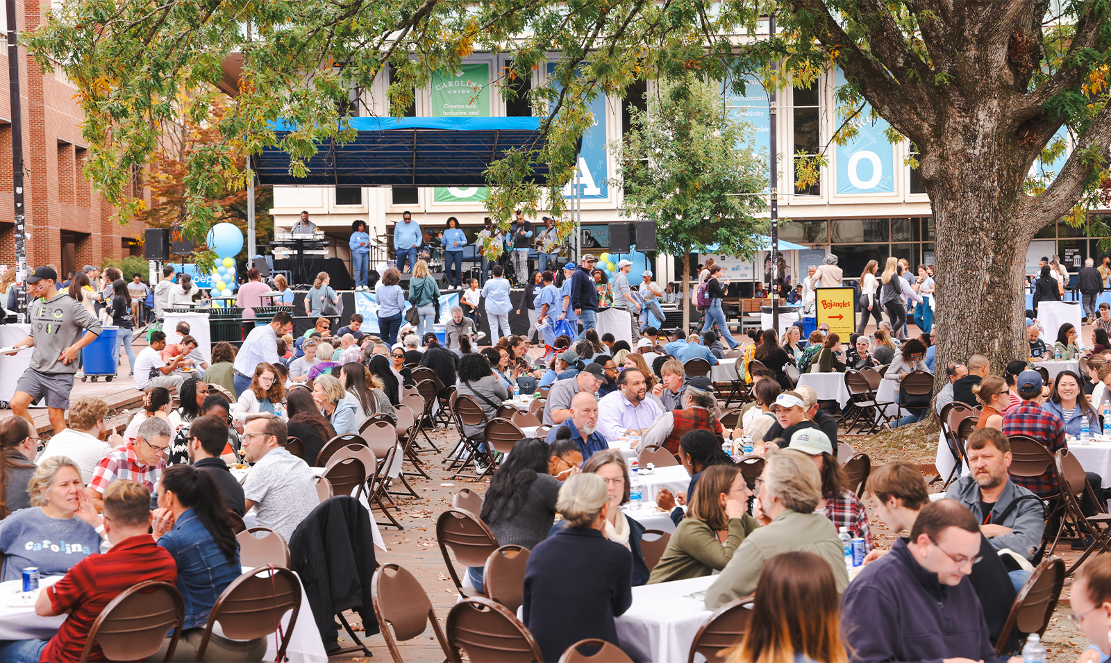 Image of a large crowd of people sitting at tables outside and eating lunch in the Pit on the campus of UNC-Chapel Hill as part of Employee Appreciation Day.