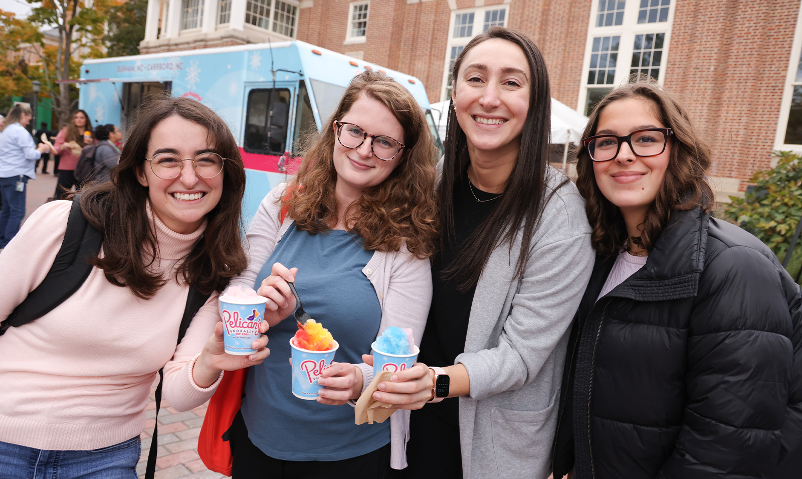 Four women posing for a photo while holding snowcones.