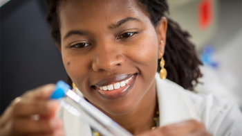 Woman smiles while examining test tube equipment.