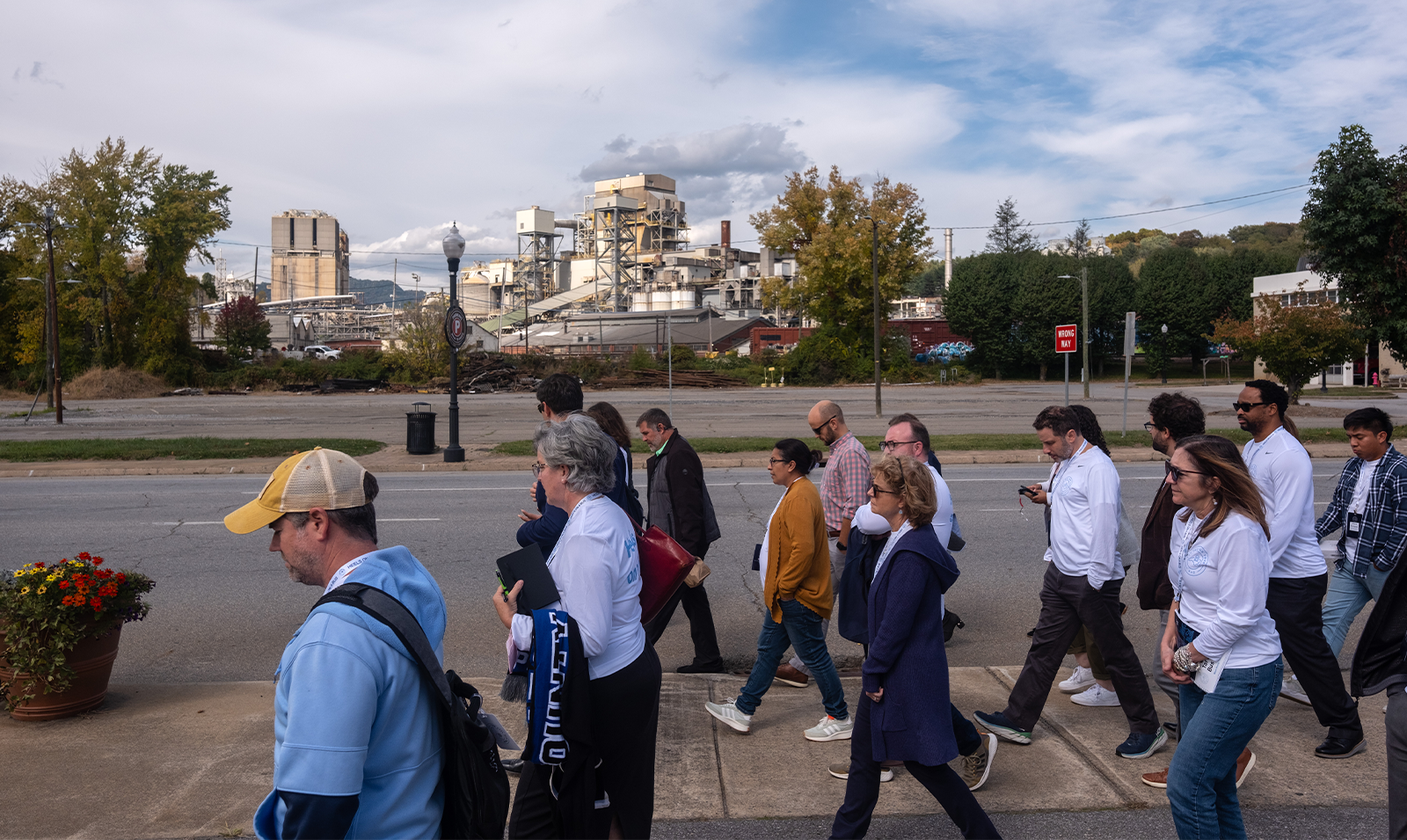 A group of Tar Heel Bus Tour participants walking down a sidwalk in downtown Canton with a recently closed down paper mill visible in the background.